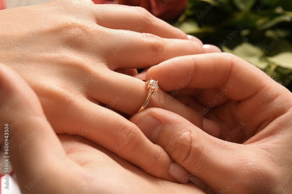 Man putting engagement ring on woman's finger, closeup