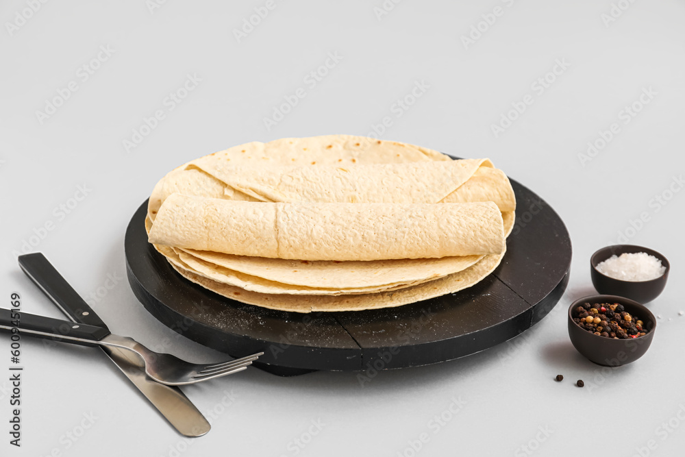 Board of thin lavash with peppercorn and salt on grey background
