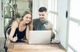 Fototapeta Tulipany - business couple Cheerful woman using laptop in coffee shop Young businessman and happy girlfriend smiling while working together Two young businessmen sit together at the table.