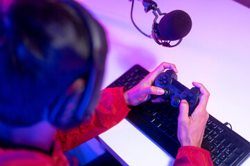 Professional gamer casting podcast walkthrough review. Young asian man sitting on chair with computer pc and microphone. Happy male Streamer wearing headphone playing game online in room neon light