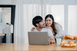 © Jirapong - Happy young loving family couple looking at laptop computer screen, reading ecipes. Wife showing embrace to husband to pretty joyful husband, sitting at table in kitchen at home in weekend.
