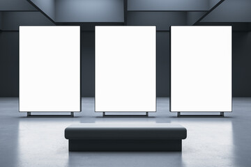 Front view on a bench on concrete floor in front of three blank white illuminated screens with place for your logo or advertising text on dark wall background in gallery hall. 3D rendering, mock up