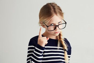 Wall Mural - Strict, serious and portrait of a child with a gesture isolated on a white background in a studio. Rude, smart and a young girl wearing glasses and gesturing with finger for discipline on a backdrop