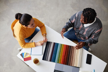 High angle view of designers using colorful palette and discussing color for future interior while sitting at table at meeting