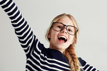 Wall Mural - Happy, excited and portrait of young girl with happiness to celebrate isolated in a white studio background. Glasses, vision and female kid smile with freedom in a strip t-shirt for child fashion