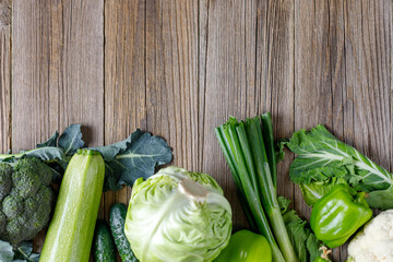 Wall Mural - Border of green raw vegetables on wooden background. Top view of healthy organic food. Copy space