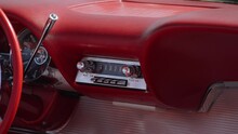 Original Old Radio In Red Leather Interior Of An Old American Car. On Dashboard Of Convertible Coupe Under Sunlight, Round Speedometer And Chrome Gear Knob.