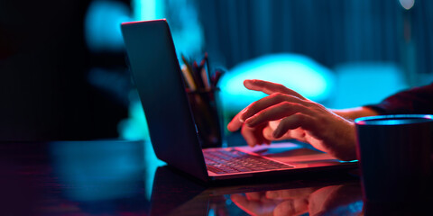 Businessman working remotely, typing on laptop keyboard over neon lights. Home office in neon lights. Concept of business, modern technologies, occupation, career development