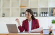 © crizzystudio - Asian businesswoman sitting happily in office holding detailed report paper analyzing data accuracy in financial matters management concept.