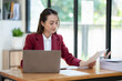 © crizzystudio - Asian businesswoman clicking details on laptop computer analyzing data checking accuracy of financial income happily in office management concept management.