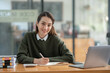 © crizzystudio - Asian businesswoman sitting in front of the computer while working at the office Looking at the camera with a smiling face Business and technology. Home office. Living concept.