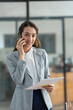 © crizzystudio - Attractive Asian businesswoman standing on the phone talking about real estate projects and chatting with happy smiles at the office.