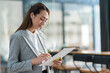 © crizzystudio - Successful smiling asian businesswoman standing holding pen checking customer data on export parcel online at office new management concept.