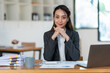 © crizzystudio - Asian businesswoman sitting in front of the computer while working at the office Looking at the camera with a smiling face Business and technology. Home office. Living concept.