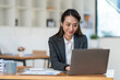 © crizzystudio - Young Asian businesswoman holding a pen sitting and analyzing the details of management information Finance is happy at the desk in the office.
