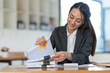 © crizzystudio - Asian businesswoman working in piles of paper files to find and review unfinished documents in the financial document folder business agreement on the desk in the office.