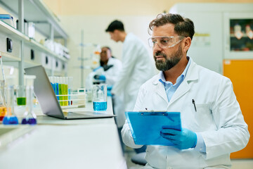 Wall Mural - male scientist taking notes while analyzing medical data on laptop in laboratory.