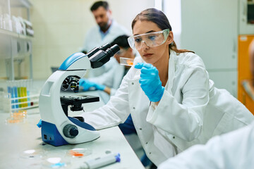 young female scientist analyzing test sample while working with microscope in lab.