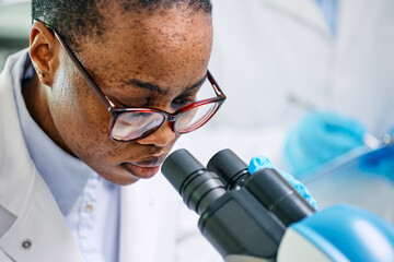 Wall Mural - black female chemist looking through microscope while working on medical research in laboratory.