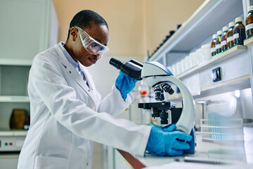 Wall Mural - black female doctor adjusting microscope during research in laboratory.
