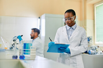 Wall Mural - Black biochemist taking notes during her research in laboratory.