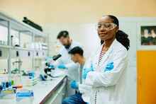 Black Biochemist Standing With Her Arms Crossed In Lab And Looking At Camera.