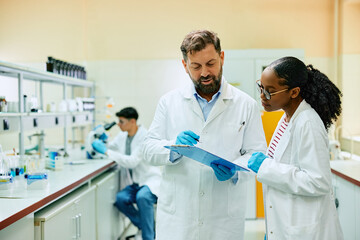 Wall Mural - Two scientists cooperating while analyzing research data in laboratory.