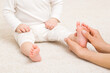Masseur hand holding infant leg and massaging foot on carpet. Baby healthcare. Closeup. Front view.