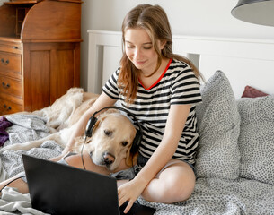 Sticker - Pretty girl with golden retriever dog, headphones and laptop in bed. Female teenager with purebred doggy pet labrador making video call at pc online