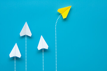 Wall Mural - Top view of yellow paper airplane origami flying to a different direction separate from other white airplanes on blue background. Leadership and business concept