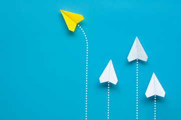 Wall Mural - Top view of yellow paper airplane origami flying to a different direction leaving other white airplanes on blue background. Leadership concept