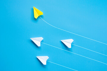 Wall Mural - Top view of yellow paper airplane origami flying to a different direction leaving other white airplanes on blue background. Leadership and direction concept
