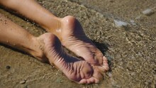 Female Bare Feet Lie In The Sea On A Sandy Beach. Close Up Bare Legs