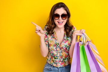 Wall Mural - Portrait of excited pretty girl hold boutique bags indicate finger empty space isolated on yellow color background