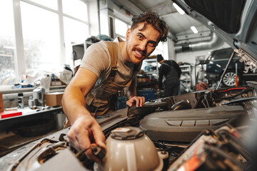 Wall Mural - Young male mechanic examining engine under hood of car at the repair garage