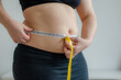Overweight woman measuring her belly with a tape measure