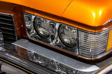 Close-up Of The Round Headlamps Of A Orange American Classic Car. Natural Patine On The Chrome Details Of A Historic Vehicle.