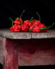 Wall Mural - Red peppers 7 Pot Brain Strain on wooden table. Handful of hot South American peppers. Table made of old wood. Dark background. Side view. Copy space.
