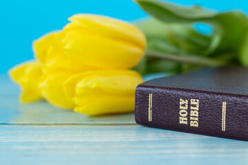 Wall Mural - Closed holy bible book and yellow tulips on wooden table with blue background. A close-up. Christian growth, hope, and faith in God Jesus Christ, biblical concept.