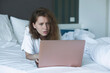 © Евгений Шемякин - young woman lies and use laptop in bed in the morning. concept online learning, work, shopping