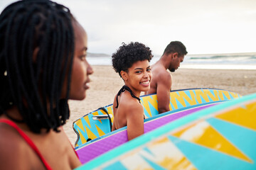 Three African American surfer friends carrying their surfboard walking on the beach