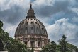 Imponująca kopuła Bazyliki Świętego Piotra w Rzymie, widziana z perspektywy Muzeum Watykańskiego. Masywne i majestatyczne struktury są symbolem historycznej i religijnej potęgi Watykanu.
