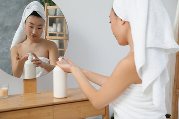 Canvas Print - Beautiful young Asian woman applying body cream on hands in bathroom