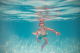 Fototapeta  - Child playing in swimming pool. Kids holidays and vacation concept. Summer kid play in swimming pool. Little child boy in pool underwater. Kids swim in pool on summer vacation.