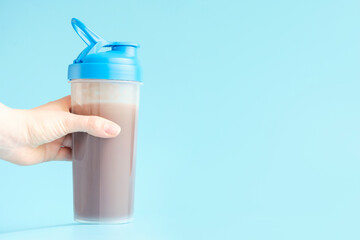 Female hand holds a shaker with protein shake on blue background.