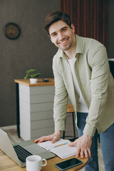 Wall Mural - Young man wears casual clothes stand near alone at table in coffee shop cafe restaurant indoors work study on laptop pc computer write in notebook drink tea. Freelance mobile office business concept.