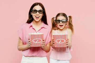 Wall Mural - Young woman wear casual clothes with child kid girl 6-7 years old in 3d glasses watch movie film hold bucket of popcorn in cinema. Mother daughter isolated on plain pink background Family day concept