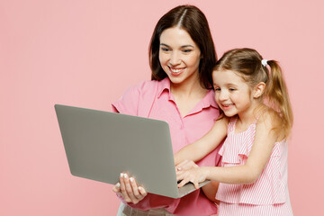 Wall Mural - Happy cheerful IT woman wear casual clothes with child kid girl 6-7 years old. Mother daughter hold use work on laptop pc computer isolated on plain pastel pink background. Family parent day concept.