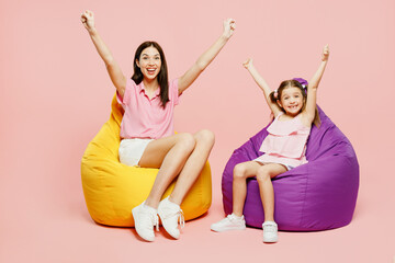 Wall Mural - Full body woman wear casual clothes with child kid girl 6-7 years old. Mother daughter sit in bag chair do winer gesture look camera isolated on plain pastel pink background Family parent day concept