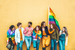 Diverse group of young people celebrating gay pride festival day - Lgbt community concept with guys and girls hugging together outdoors - Multiracial trendy friends standing on a yellow background
